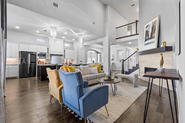 living area with dark wood-style floors, visible vents, a fireplace, and a high ceiling