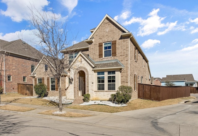 view of front of home with stone siding, brick siding, fence, and roof with shingles