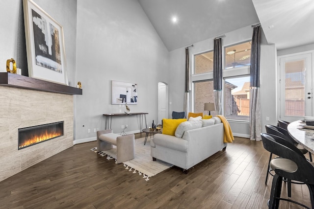 living area with arched walkways, high vaulted ceiling, a stone fireplace, and wood finished floors