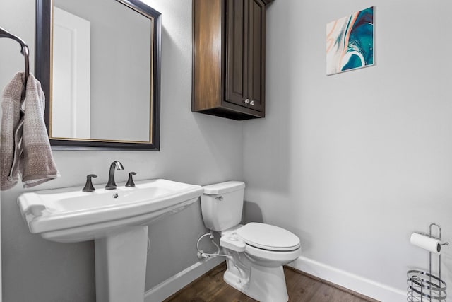 half bathroom with baseboards, a sink, toilet, and wood finished floors