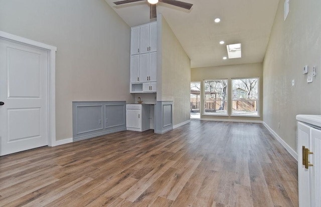 unfurnished living room featuring a high ceiling, ceiling fan, light hardwood / wood-style floors, and a skylight