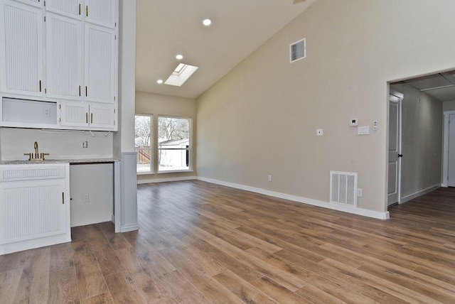 kitchen featuring white cabinets, a skylight, sink, and light wood-type flooring