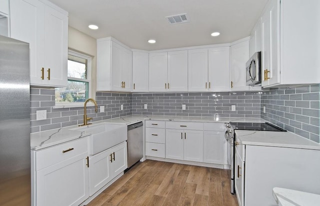 kitchen with stainless steel appliances, sink, white cabinets, and light hardwood / wood-style flooring