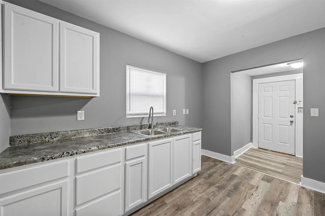 kitchen with dark stone countertops, sink, light hardwood / wood-style flooring, and white cabinets