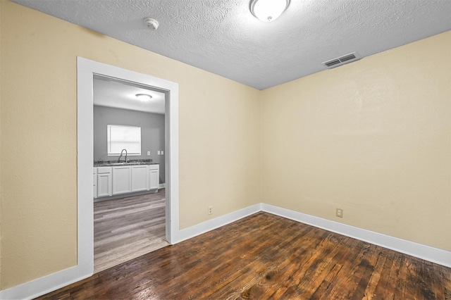 unfurnished room featuring dark hardwood / wood-style floors, sink, and a textured ceiling