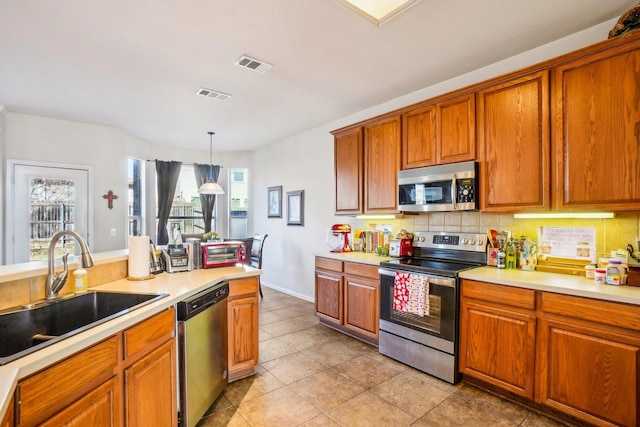 kitchen with sink, light tile patterned floors, appliances with stainless steel finishes, hanging light fixtures, and decorative backsplash