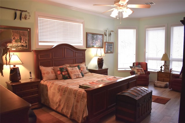 bedroom featuring a ceiling fan, visible vents, crown molding, and wood finished floors