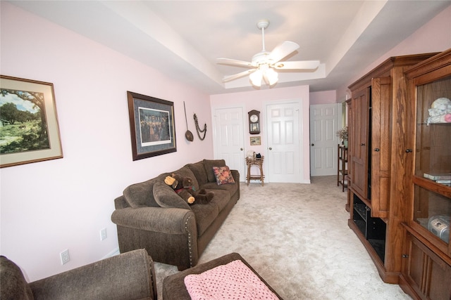 living room featuring ceiling fan, a tray ceiling, and light colored carpet