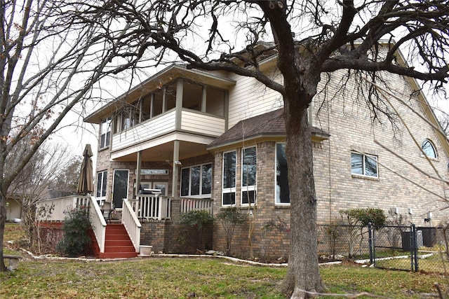 view of front facade with brick siding, fence, roof with shingles, a gate, and a front lawn