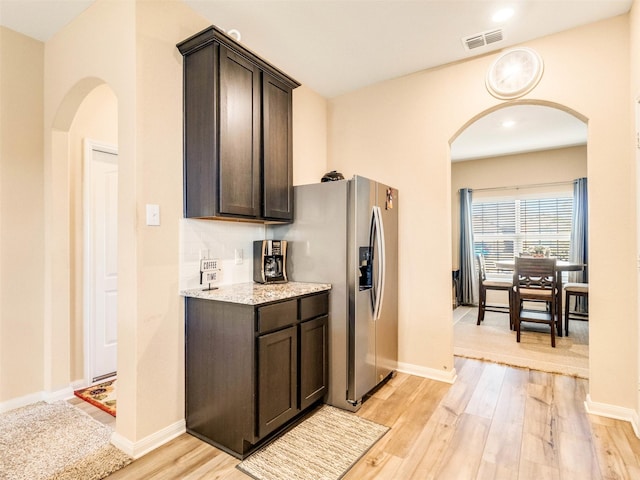 kitchen with light stone countertops, dark brown cabinets, light hardwood / wood-style floors, and stainless steel refrigerator with ice dispenser