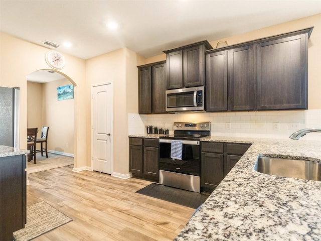 kitchen with stainless steel appliances, sink, dark brown cabinetry, and light hardwood / wood-style floors