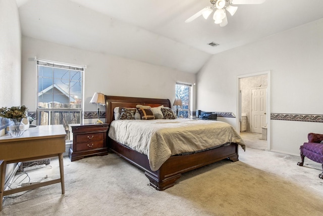 bedroom with vaulted ceiling, light colored carpet, ceiling fan, and ensuite bath