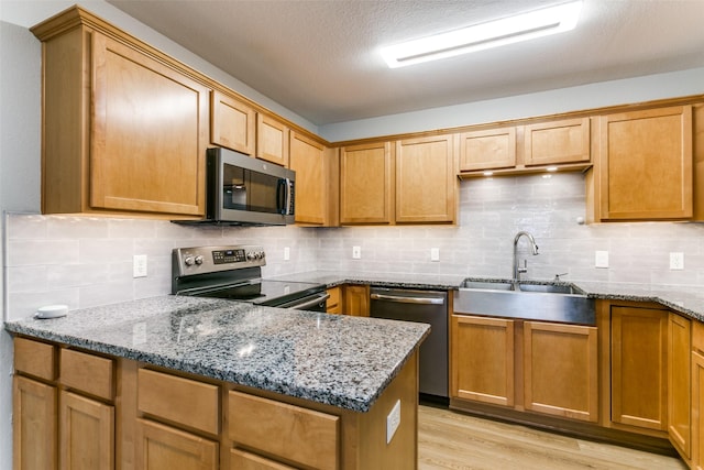 kitchen with appliances with stainless steel finishes, stone countertops, sink, backsplash, and light hardwood / wood-style floors