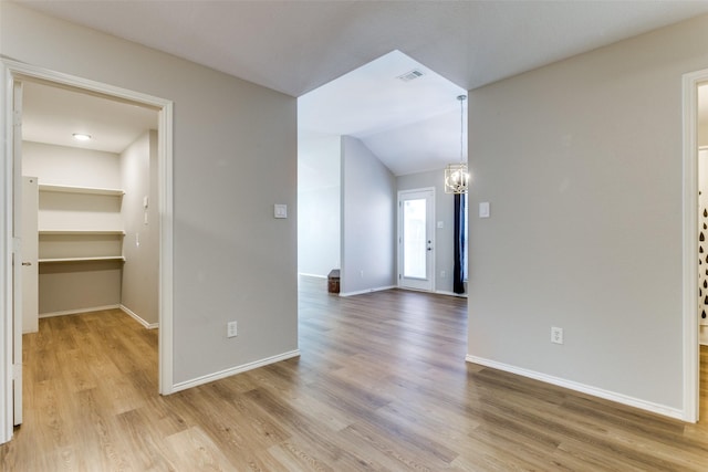 unfurnished room with lofted ceiling, a notable chandelier, and light hardwood / wood-style floors