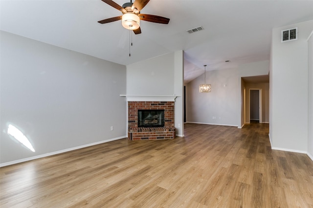 unfurnished living room featuring lofted ceiling, ceiling fan with notable chandelier, a brick fireplace, and light wood-type flooring