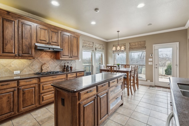 kitchen with light tile patterned flooring, a center island, ornamental molding, pendant lighting, and backsplash