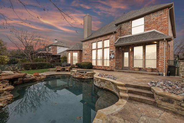 pool at dusk with an in ground hot tub and a patio