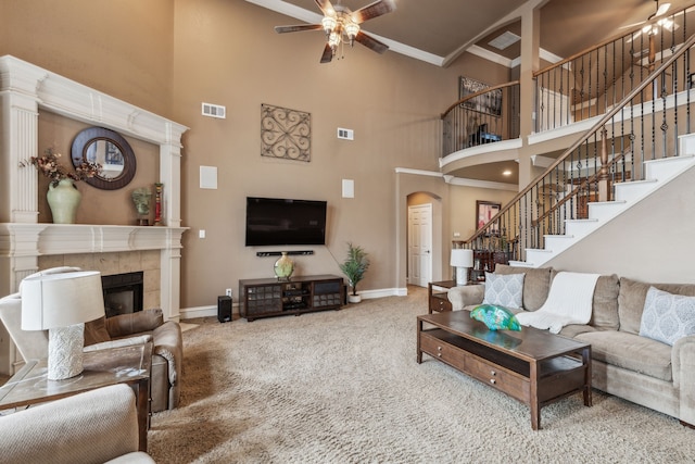 carpeted living room featuring crown molding, a towering ceiling, a fireplace, and ceiling fan