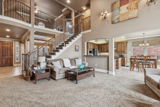 tiled living room with a towering ceiling, ornamental molding, and ceiling fan with notable chandelier