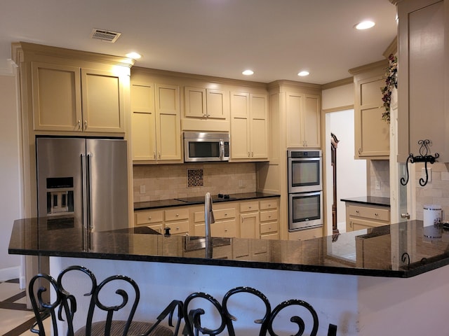 kitchen featuring a breakfast bar, appliances with stainless steel finishes, kitchen peninsula, and dark stone counters