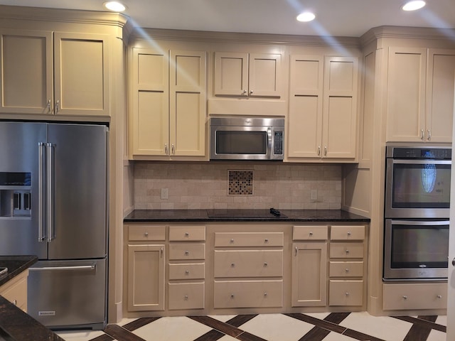 kitchen with backsplash, appliances with stainless steel finishes, light tile patterned floors, and dark stone counters