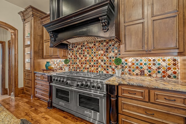 kitchen featuring premium range hood, double oven range, light stone counters, and light wood-type flooring