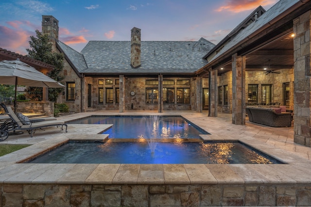 pool at dusk featuring an in ground hot tub, ceiling fan, an outdoor living space, and a patio