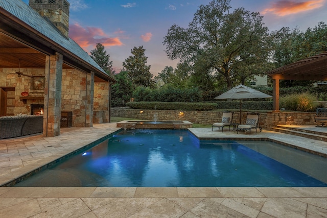 pool at dusk featuring a patio area, an outdoor stone fireplace, and an in ground hot tub