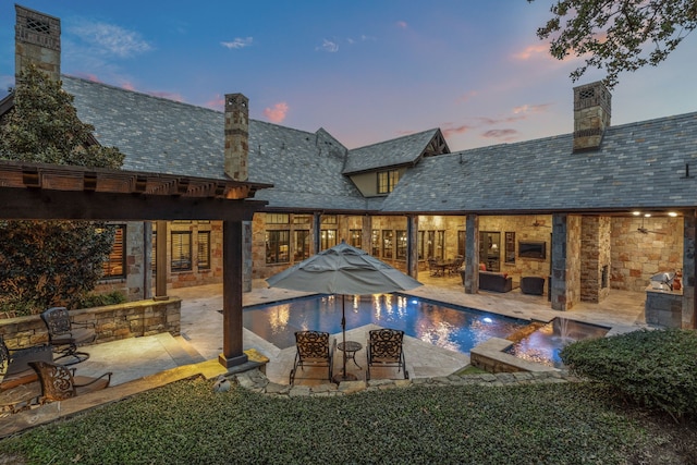 pool at dusk featuring pool water feature and a patio area