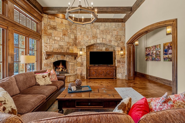 living room with a stone fireplace, hardwood / wood-style floors, a notable chandelier, and beam ceiling