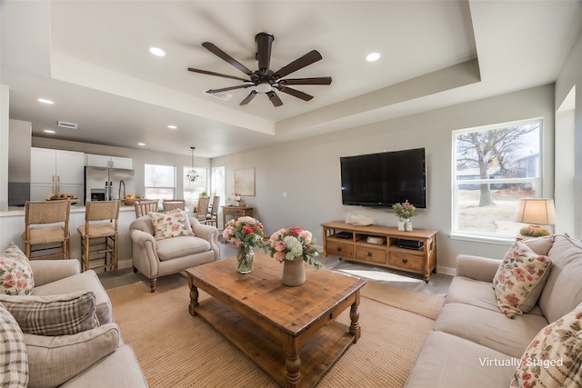 living room featuring a raised ceiling and ceiling fan