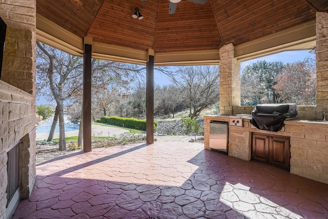 view of patio featuring ceiling fan, a gazebo, a water view, a grill, and exterior kitchen