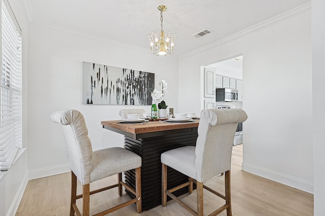 dining room with a notable chandelier, crown molding, and light hardwood / wood-style flooring