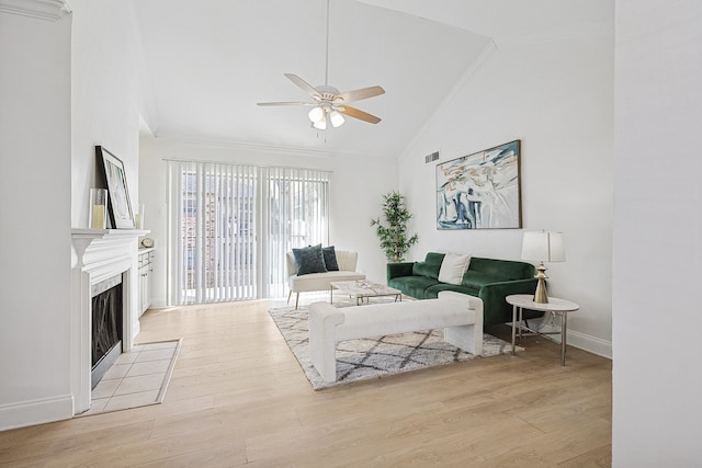 living room with a tile fireplace, high vaulted ceiling, ceiling fan, and light hardwood / wood-style flooring