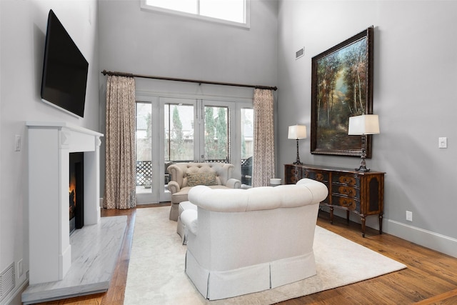 living room featuring a fireplace, light hardwood / wood-style floors, a high ceiling, and french doors