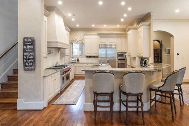 kitchen featuring a breakfast bar area, custom exhaust hood, built in appliances, kitchen peninsula, and backsplash