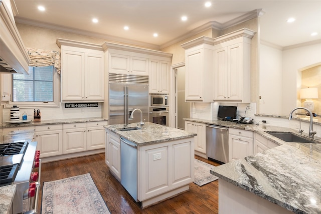 kitchen featuring an island with sink, light stone countertops, sink, and built in appliances