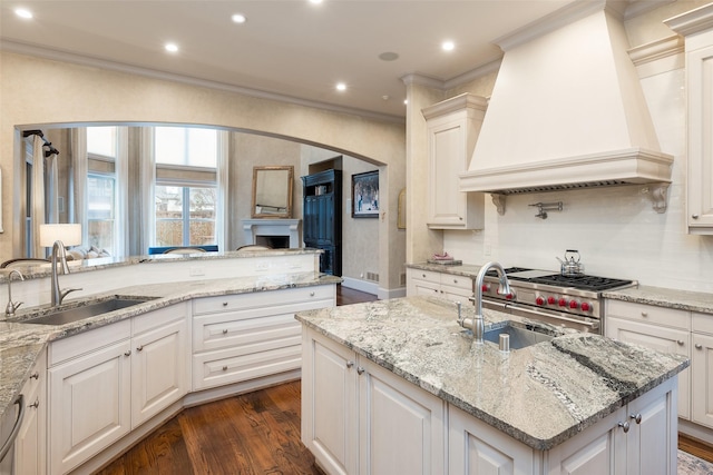 kitchen with light stone counters, sink, custom range hood, and white cabinets