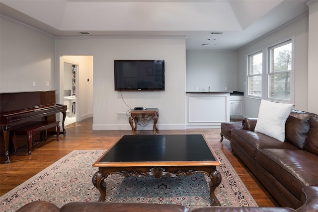 living room featuring crown molding, a tray ceiling, and light hardwood / wood-style flooring