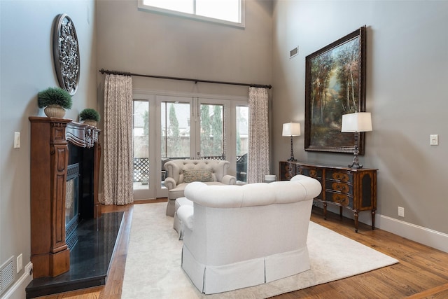 living room featuring a high end fireplace, light hardwood / wood-style flooring, french doors, and a high ceiling