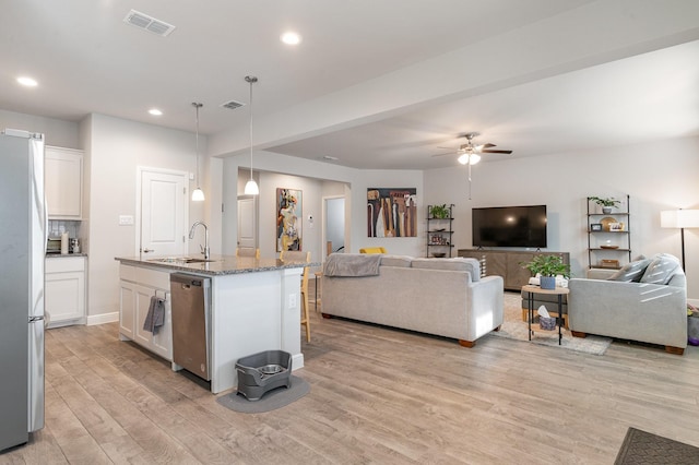 kitchen with white cabinetry, hanging light fixtures, an island with sink, stone counters, and stainless steel appliances