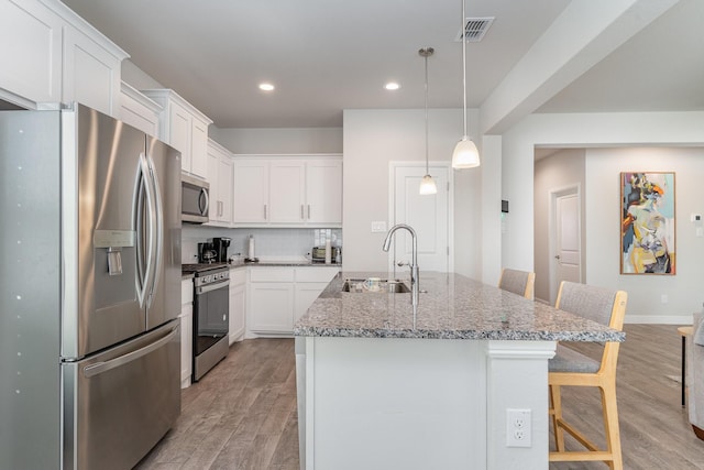 kitchen with sink, white cabinetry, a kitchen island with sink, stainless steel appliances, and a kitchen bar