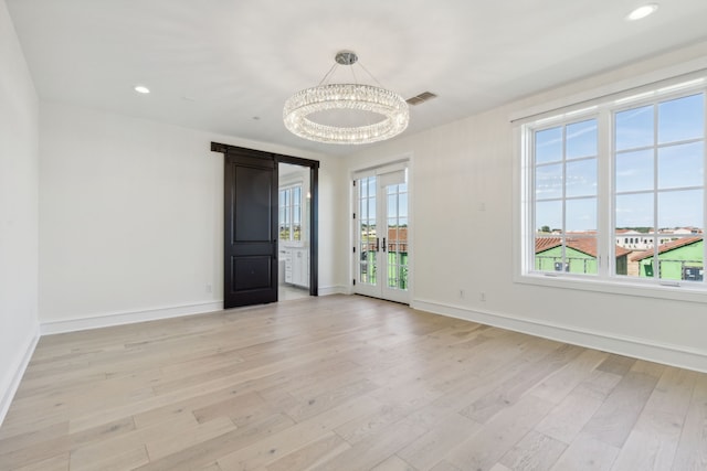 unfurnished room with an inviting chandelier, light wood-type flooring, and french doors