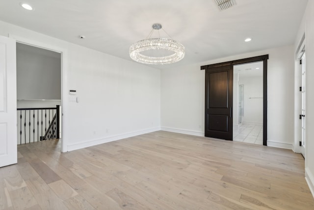 unfurnished room with a barn door, a notable chandelier, and light wood-type flooring