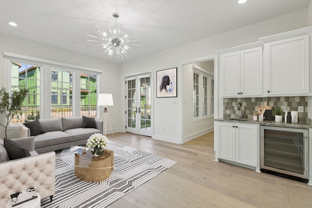 living room featuring sink, an inviting chandelier, wine cooler, french doors, and light wood-type flooring