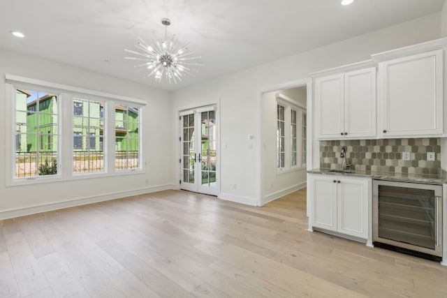 unfurnished dining area with an inviting chandelier, sink, light hardwood / wood-style flooring, and beverage cooler