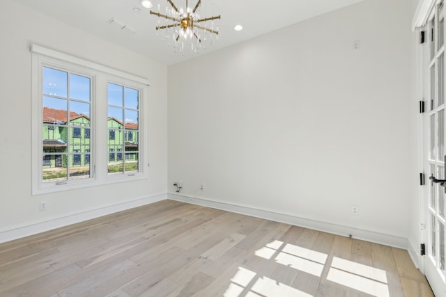 unfurnished room featuring a notable chandelier and light hardwood / wood-style flooring