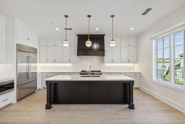 kitchen with sink, light hardwood / wood-style flooring, an island with sink, pendant lighting, and stainless steel appliances