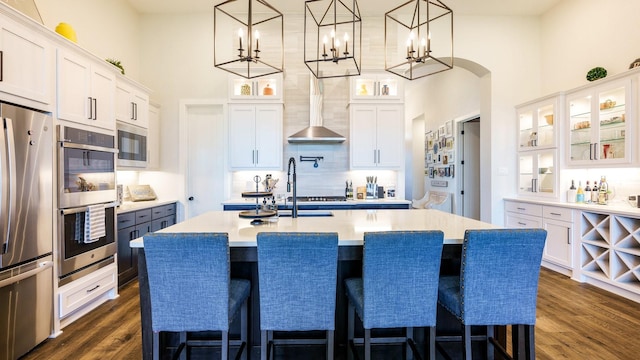 kitchen featuring appliances with stainless steel finishes, light countertops, wall chimney range hood, and dark wood-style flooring