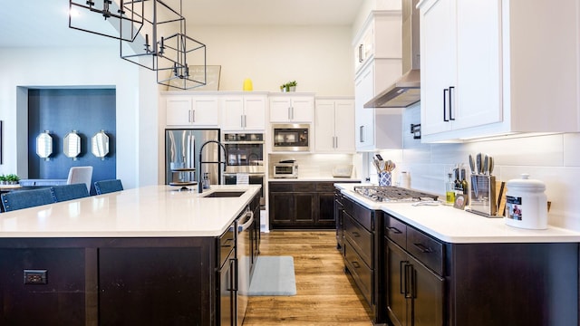 kitchen with wall chimney exhaust hood, white cabinetry, tasteful backsplash, an island with sink, and light hardwood / wood-style floors